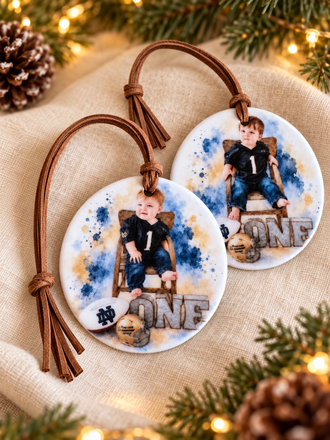 Two personalized watercolor photo ornaments with a baby in a Notre Dame outfit, printed on round ceramic with brown tassel cords