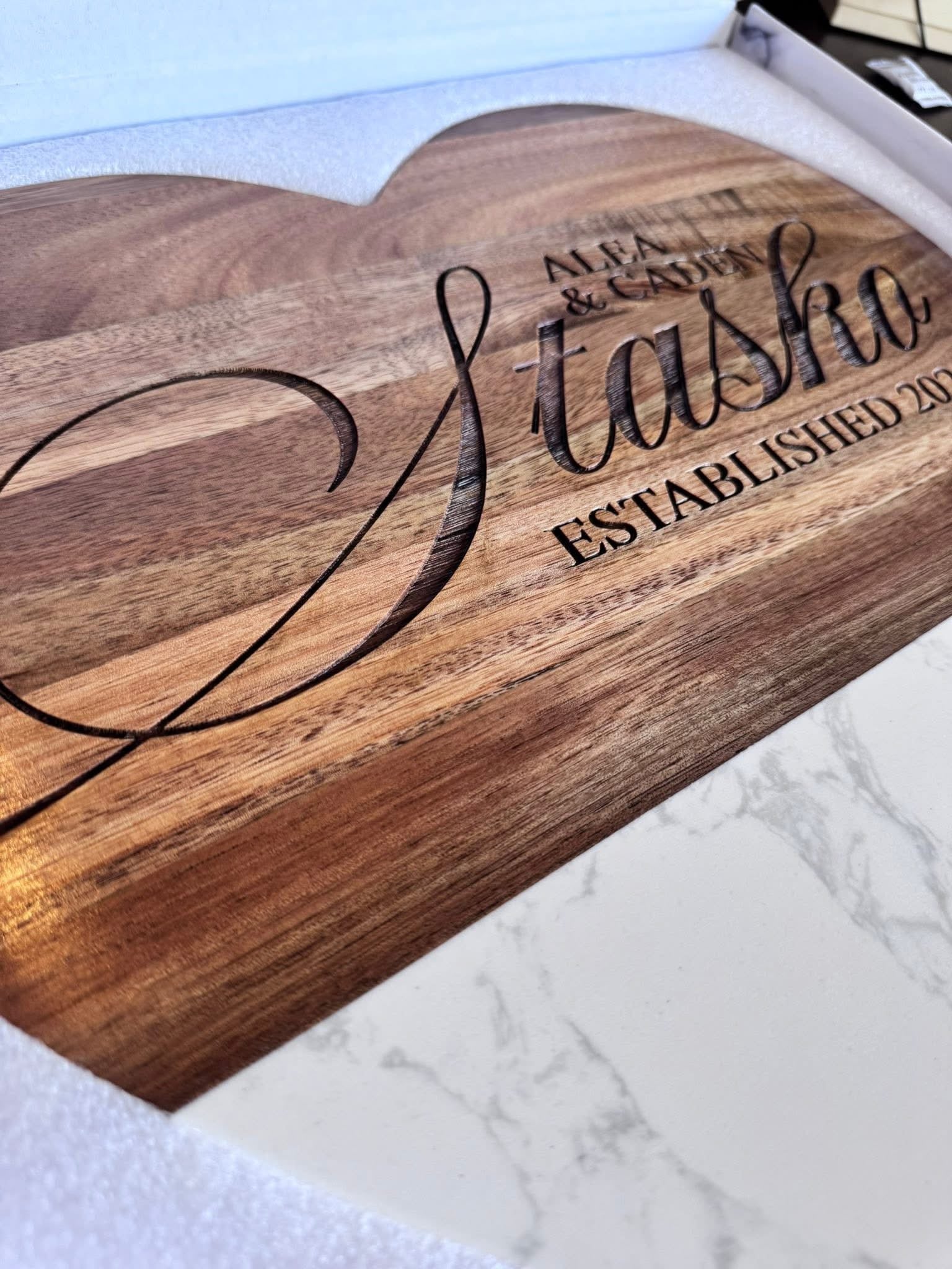 Wooden cutting board with engraved text on a marble surface